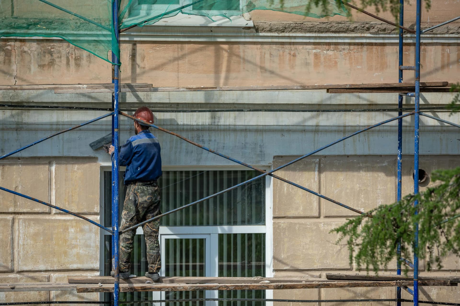 Construction worker standing on scaffolding while repairing and plastering a commercial building's exterior wall