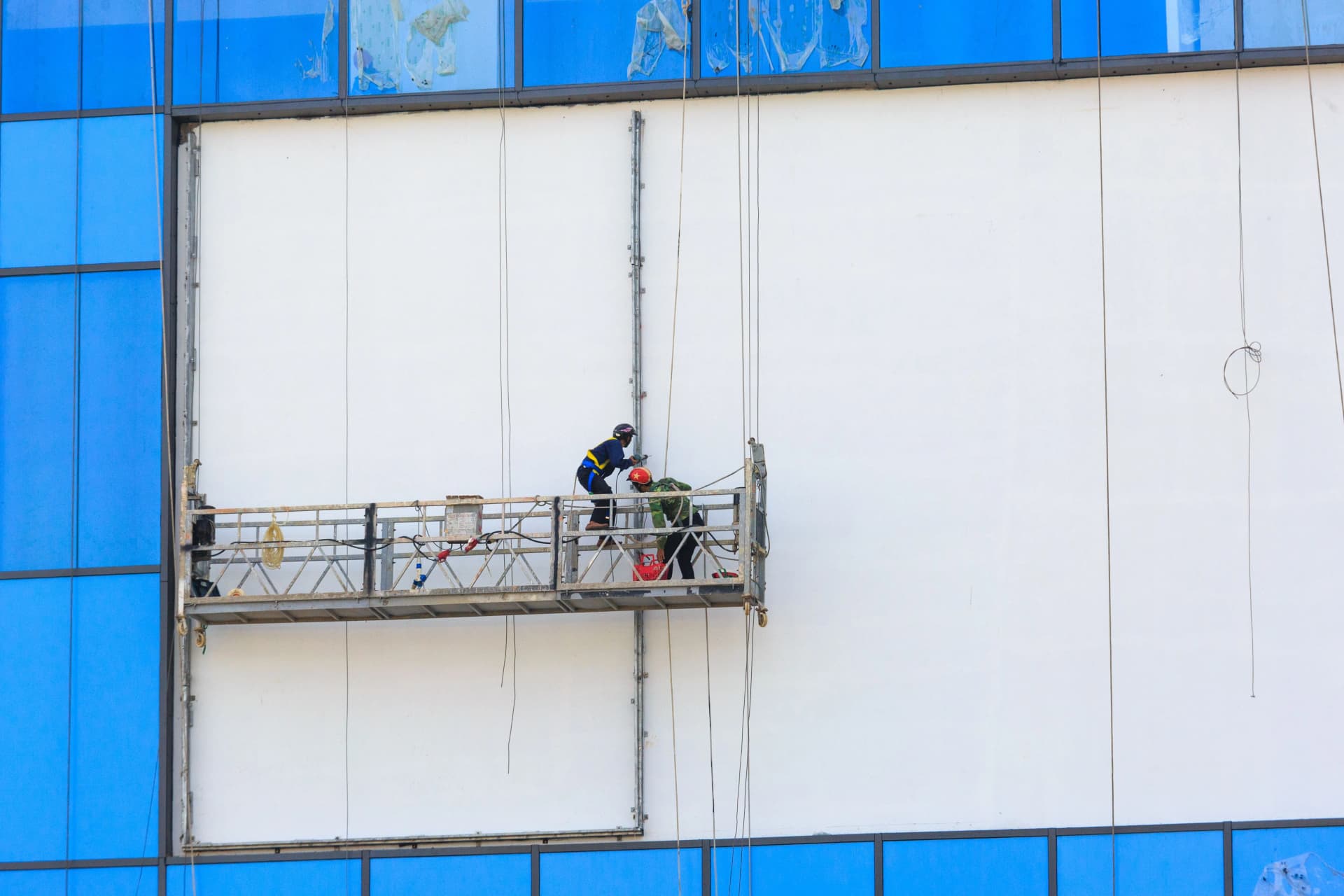 Two construction workers repairing and painting a building façade from scaffolding.