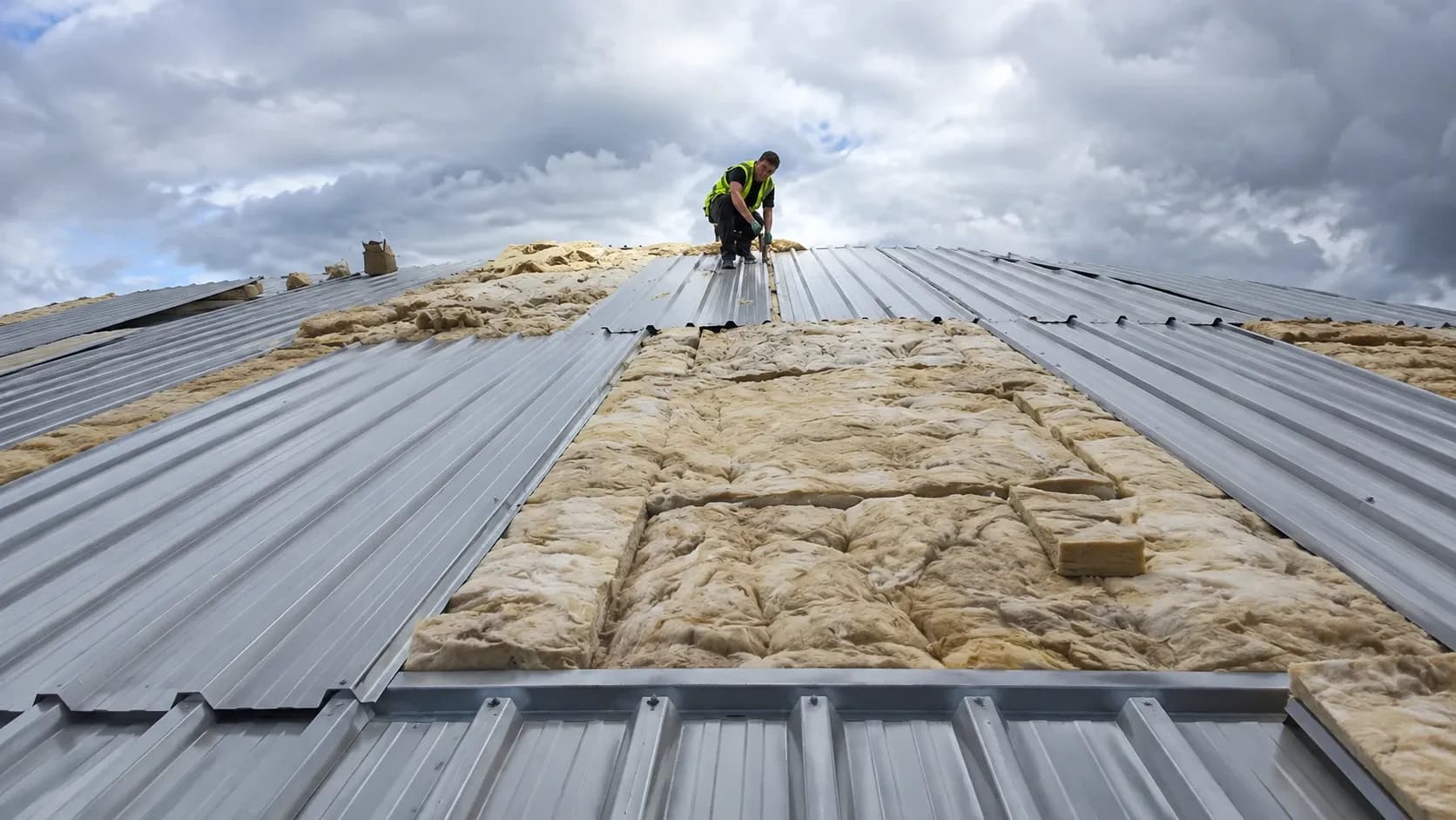 Industrial roofer installing corrugated metal roof cladding with insulation