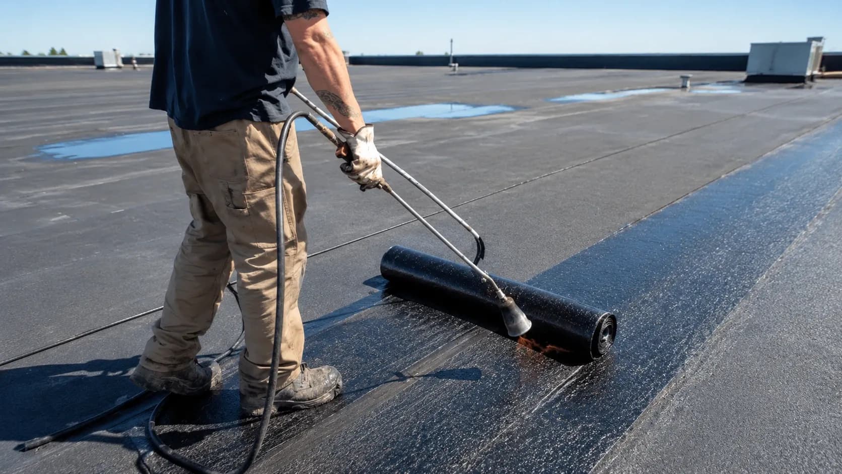 Roofer applying a bitumen membrane during flat roof construction
