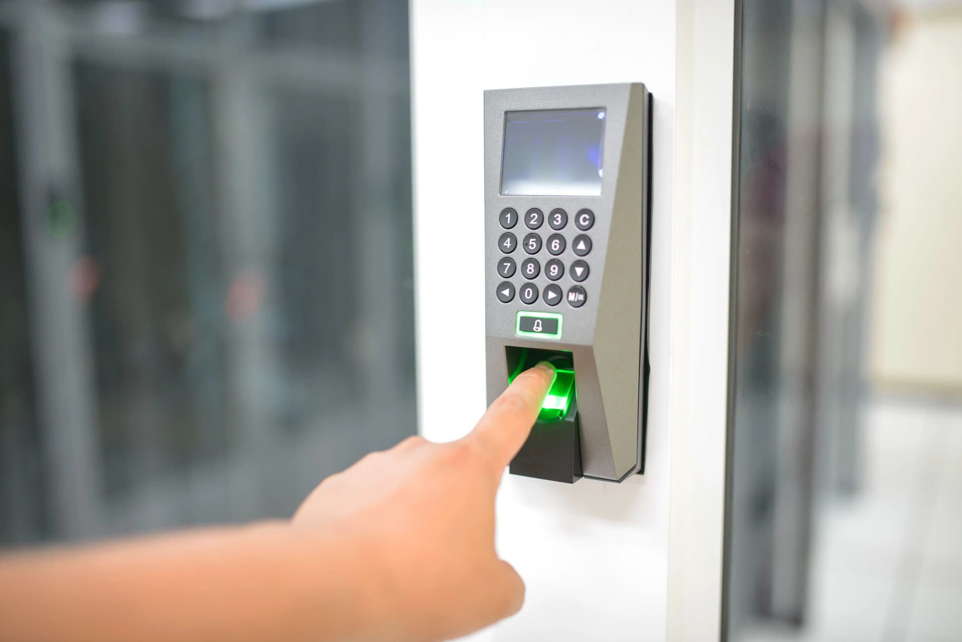 Person scanning their index finger on biometric keypad lock mounted on a white wall.
