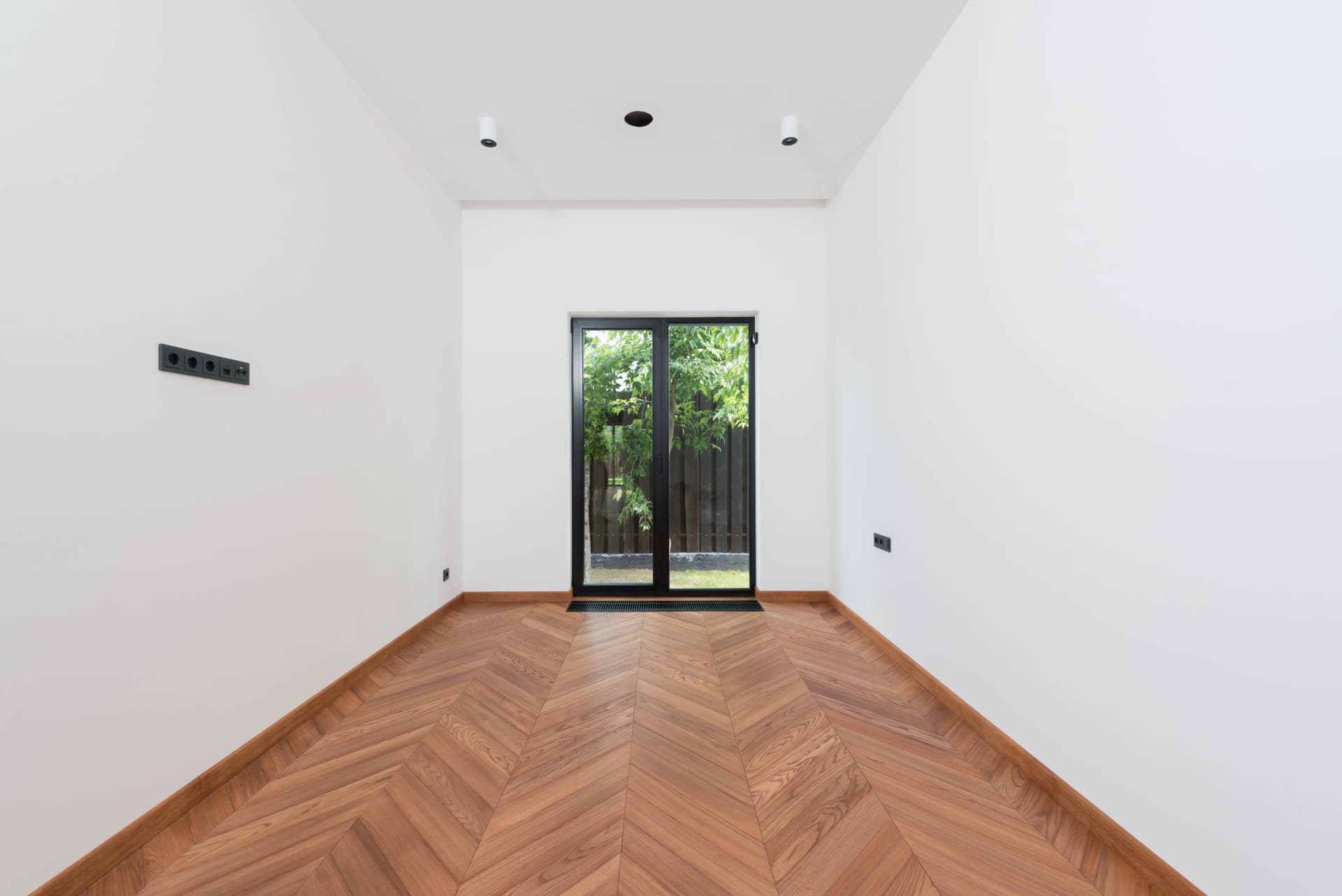 Minimalist empty room featuring white walls, herringbone wood flooring, and a glass patio door.