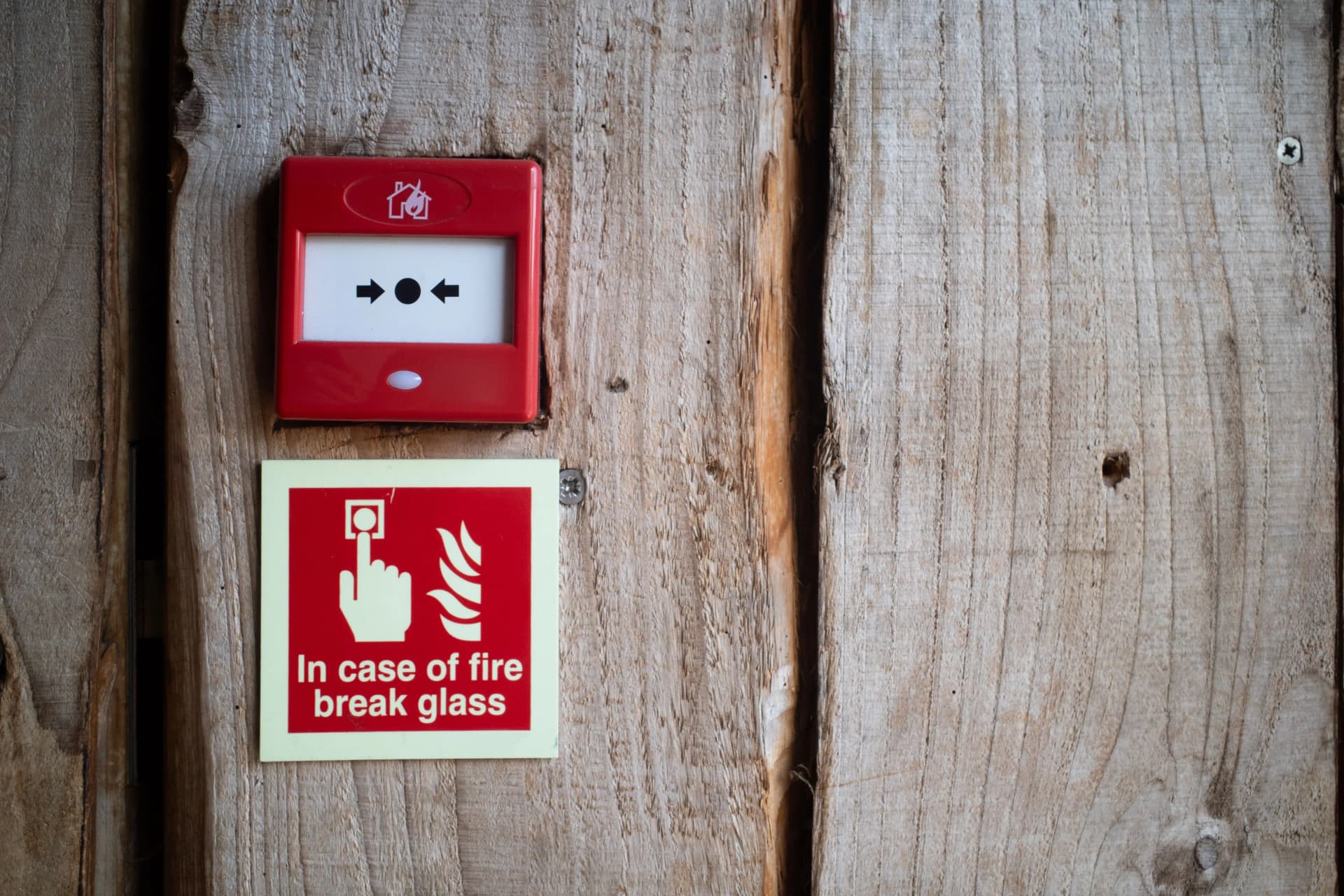 Red fire alarm call point and emergency fire signage installed on a commercial building wall.