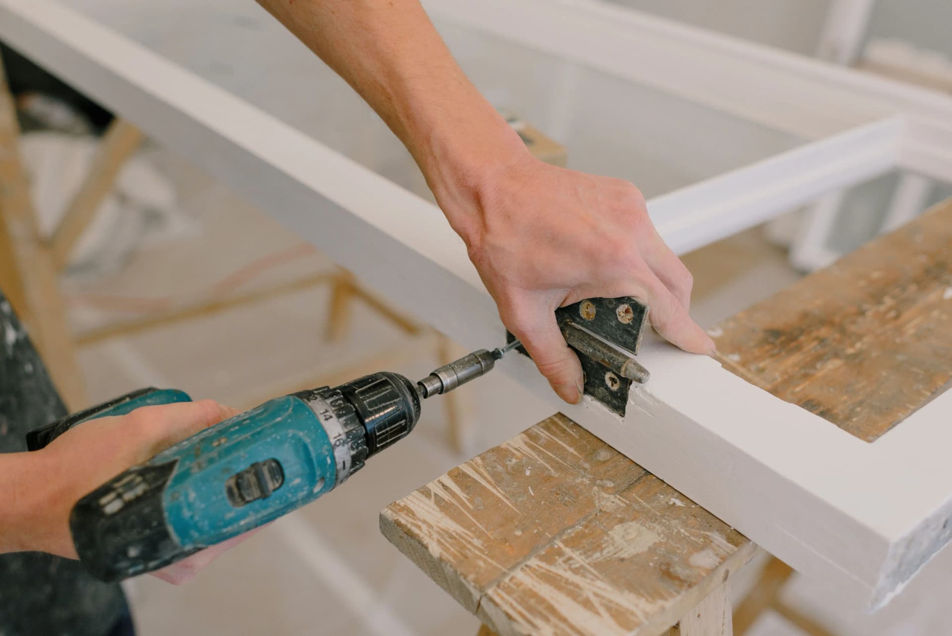 worker using a drill for furniture fittings on a wooden frame indoors.