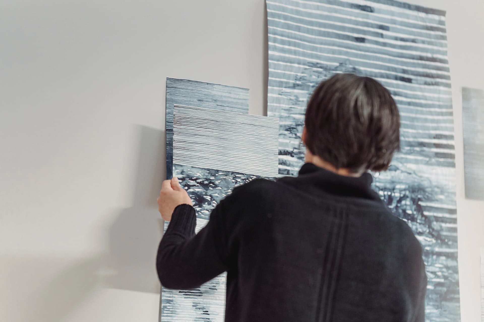 Person from behind hanging blue striped wallpaper on a plain white wall.