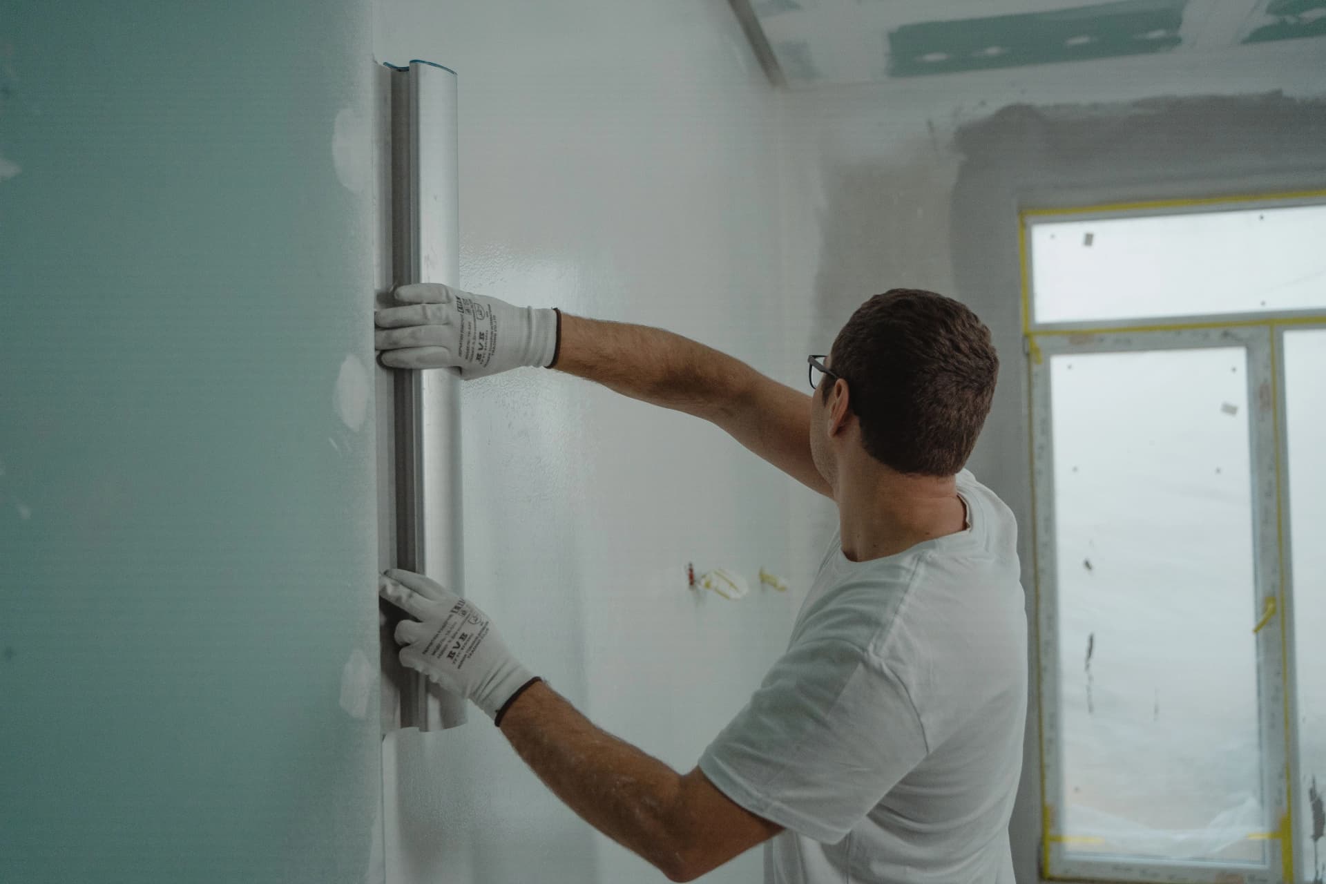 Construction worker in gloves using a large smoothing trowel on a fresh wall surface.