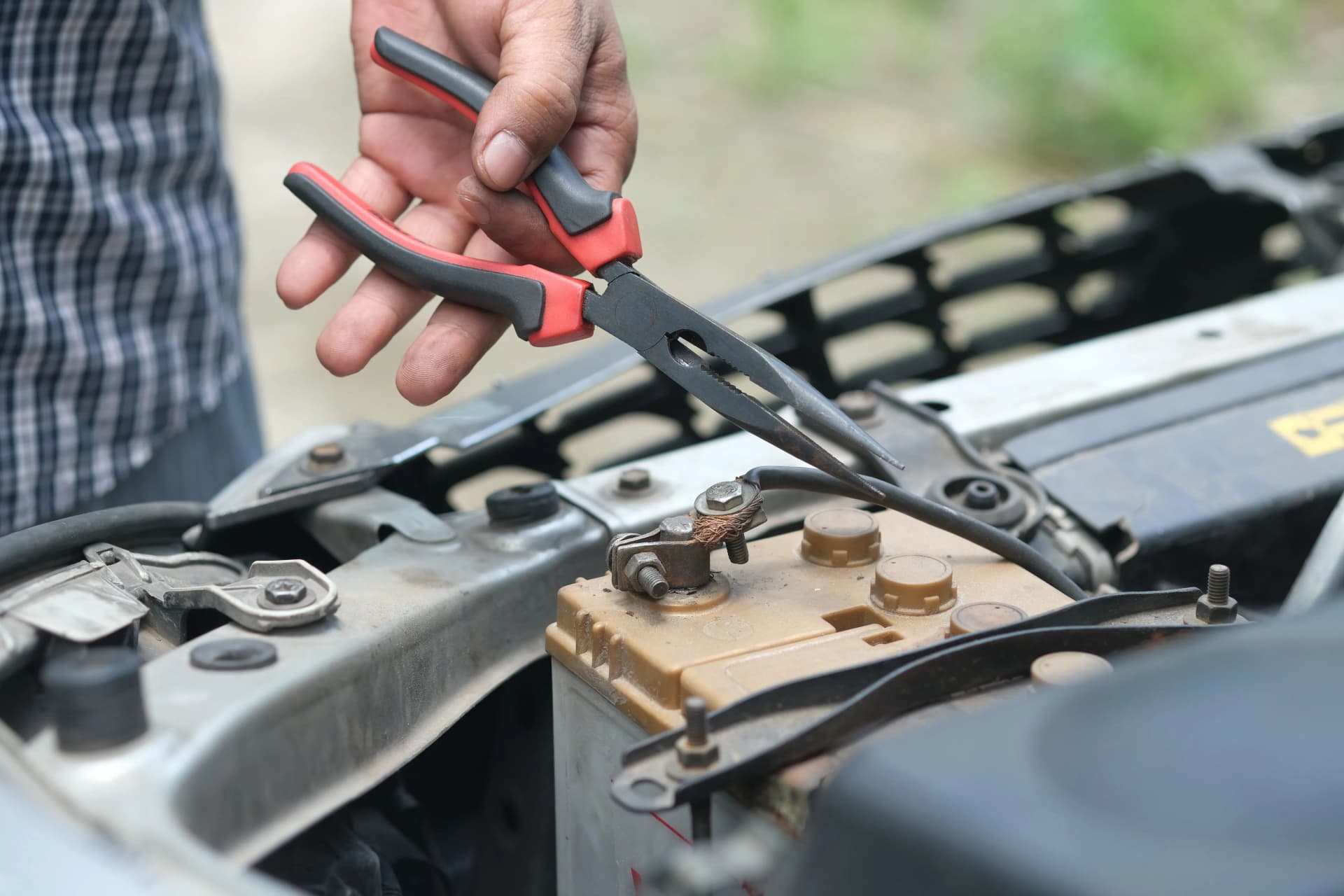 Technician carrying out maintenance work on a vehicle battery using hand tools.
