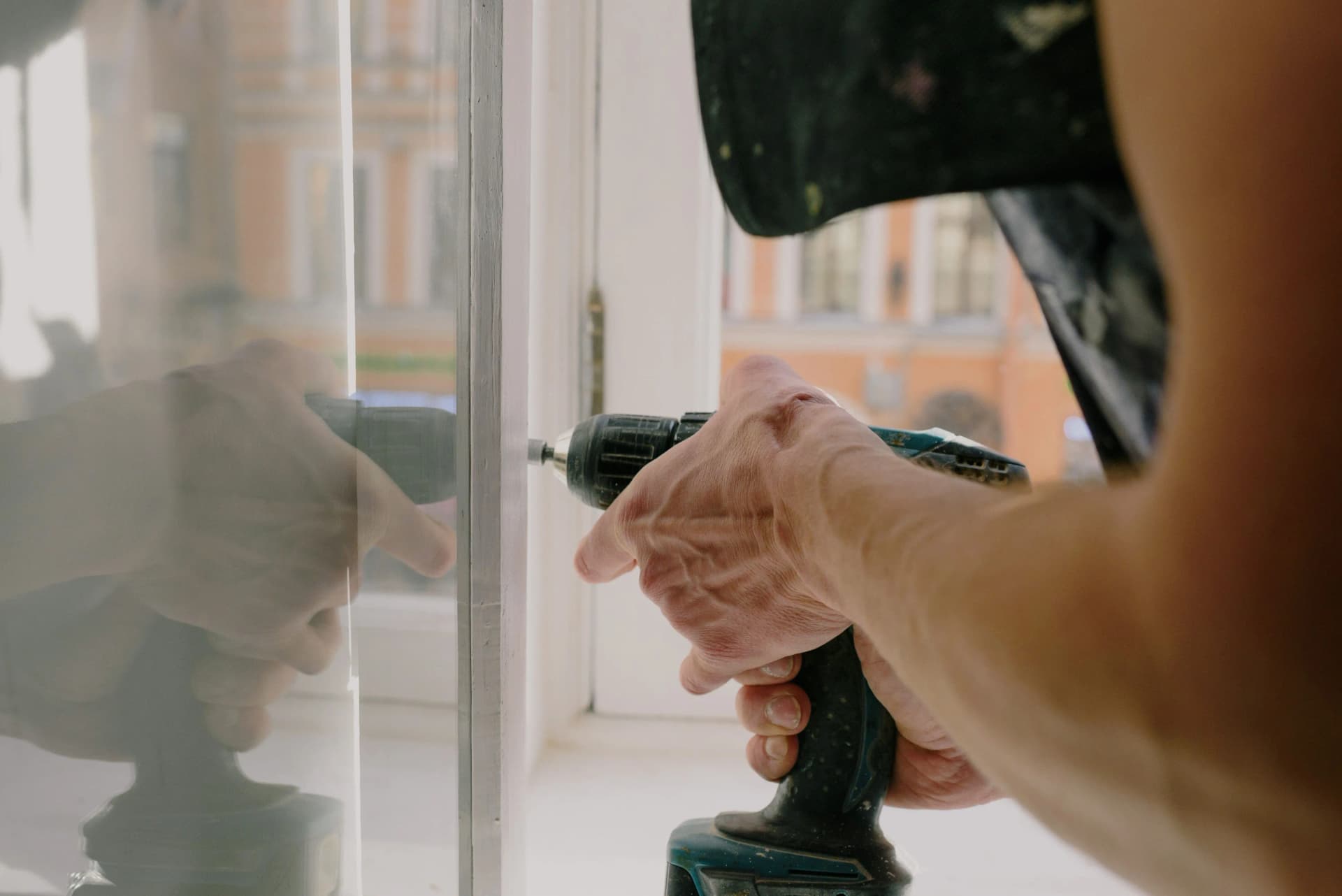 Close-up of a worker using a power drill on a wooden window frame.